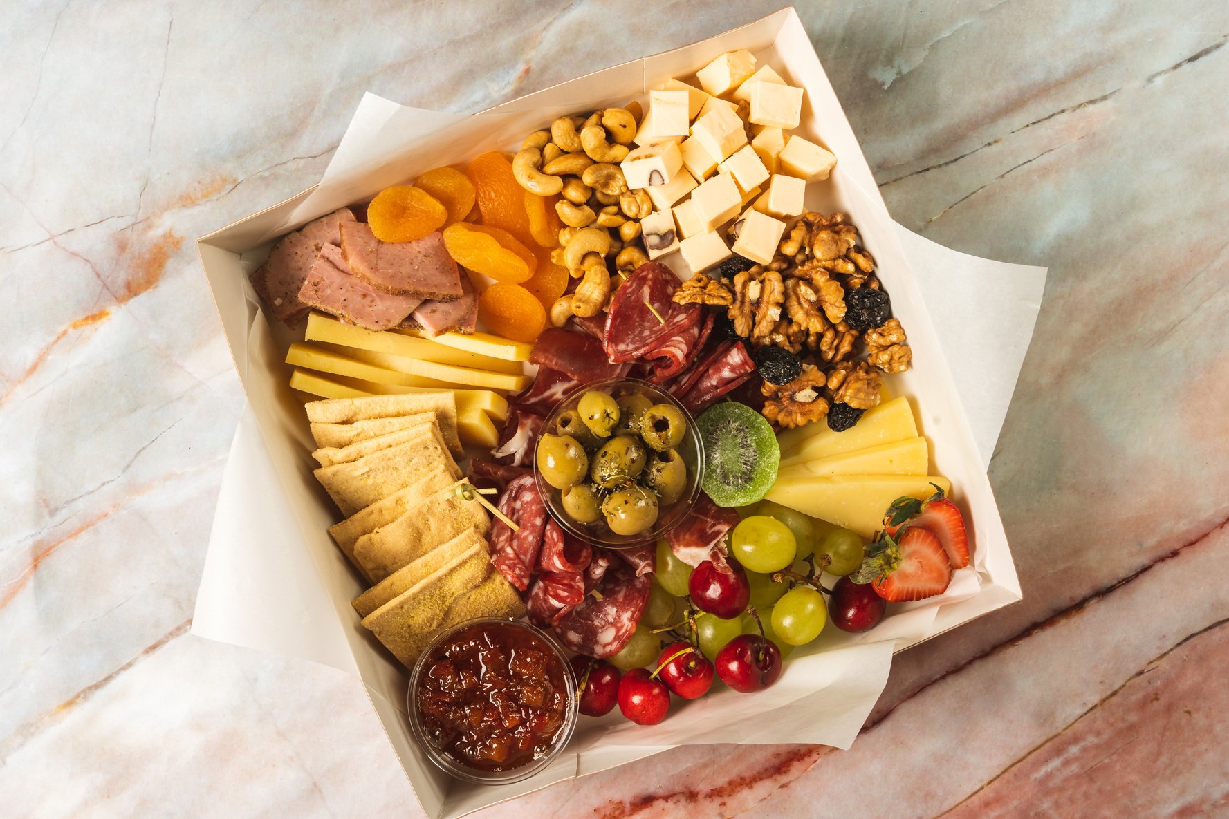 charcuterie box with cheeses, crackers, strawberries, olives, grapes, cherries, pastrami, salami, apricot and walnuts